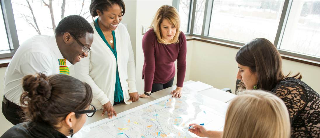 Faculty members standing around a table with a large map laid out on it.